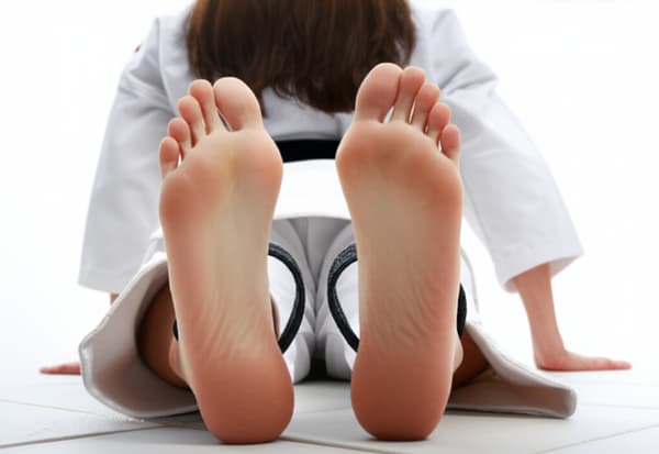 Vernis rouge sur les ongles, des tongs noires à côté des pieds, un bas de kimononde karaté blanc