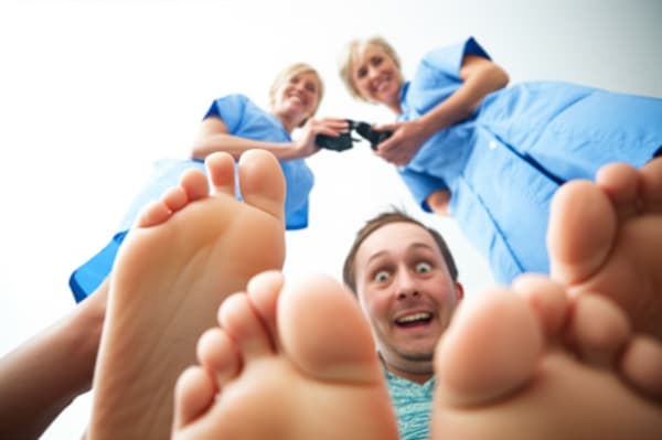 Create an image of two mature 40 year old women, have their barefeet raised above a young looking 25 year old autistic man with short brown hair and big blue eyes, have them crush/stomp him under their barefeet, a shrink ray gun is in the first woman's hands. They are both grinning.